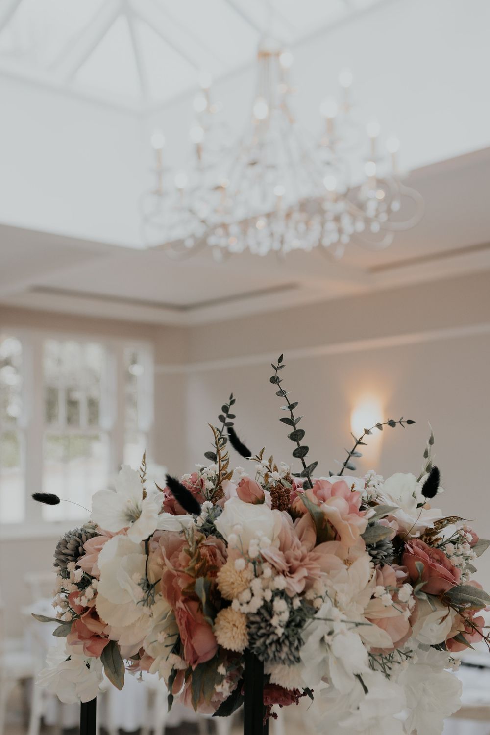 Elegant wedding centerpiece with blush pink and white flowers under a crystal chandelier.