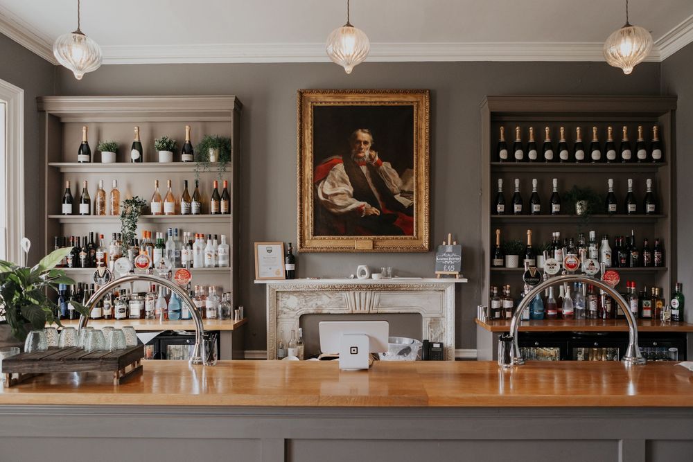 Sophisticated wedding venue bar with wood counter, portrait painting, and stocked shelves.