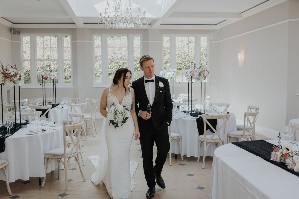 Bride and groom walking through elegantly decorated white wedding reception hall.