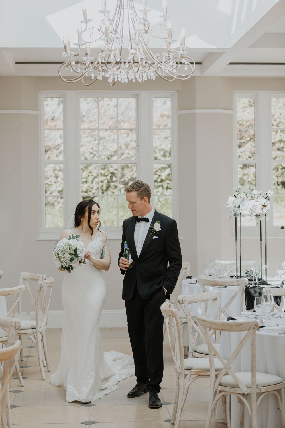 Bride and groom sharing a quiet moment in a sunlit white wedding reception hall.