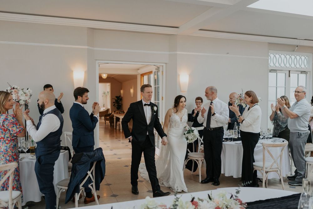 Wedding couple entering reception hall to applause from celebrating guests.