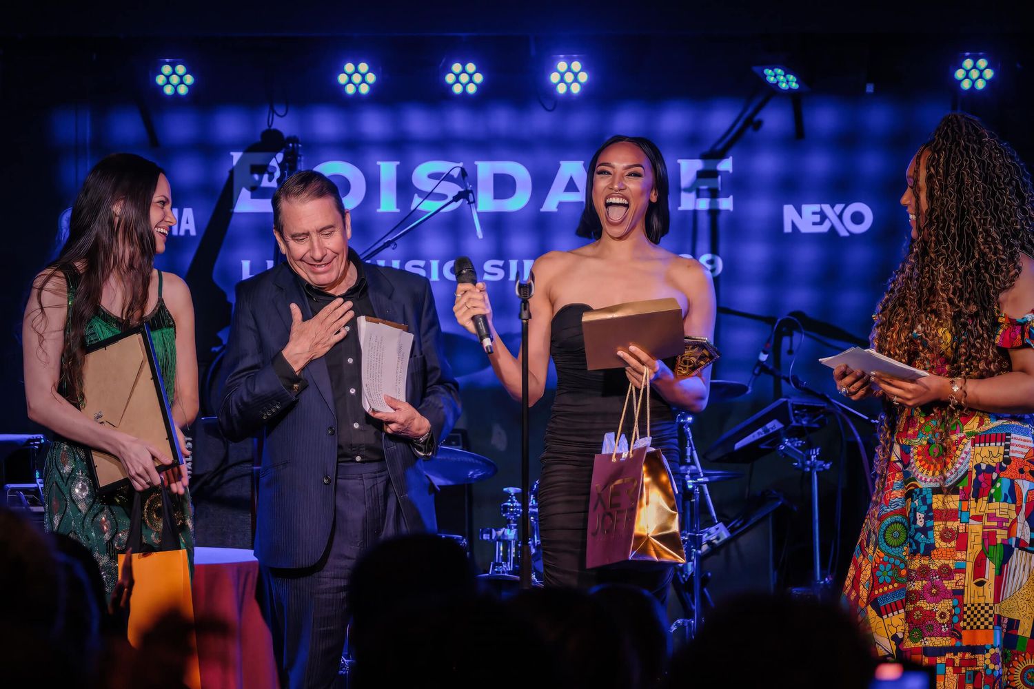 Musicians performing on stage at a jazz club with blue lighting and instruments visible in the background.