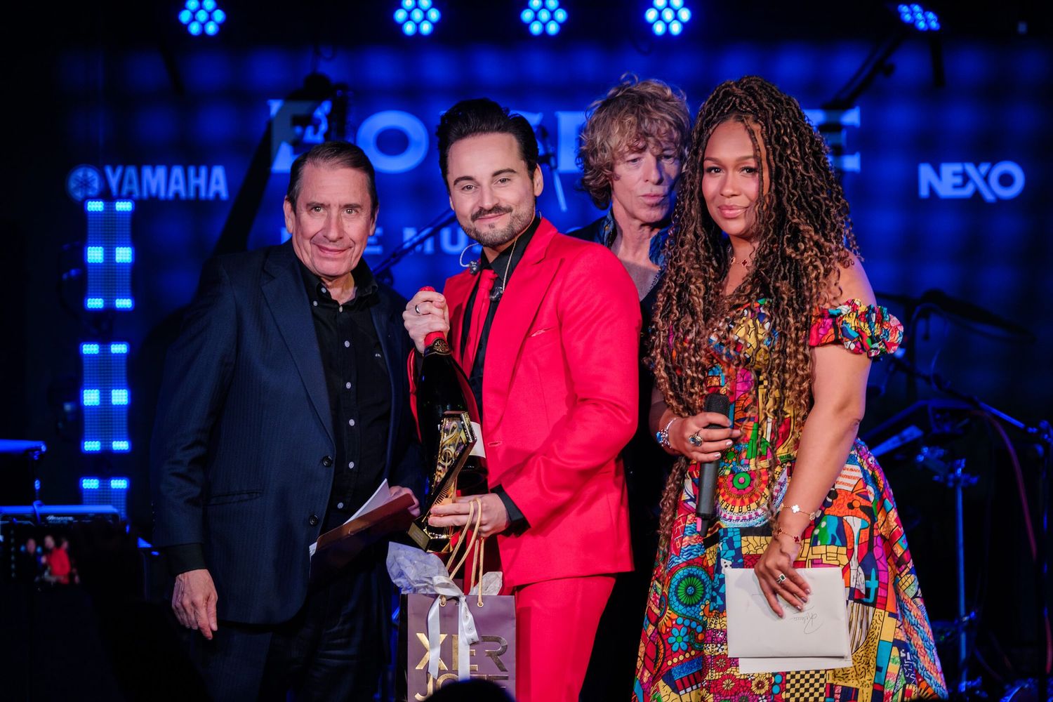 Concert performers and crew members gather backstage with blue lighting and Yamaha equipment visible in the background.