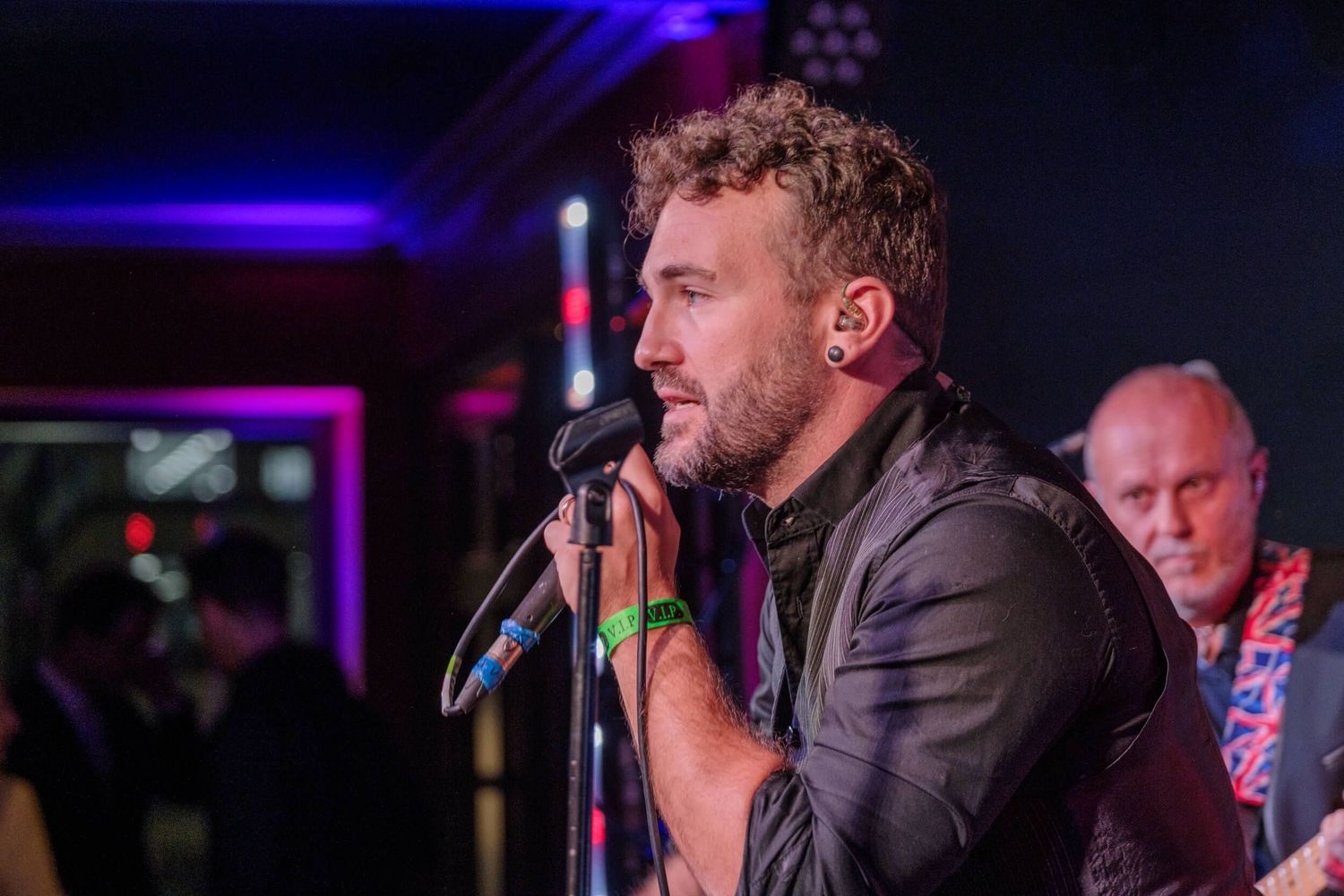 A performer sings into a microphone on stage with purple lighting in the background during a live performance.