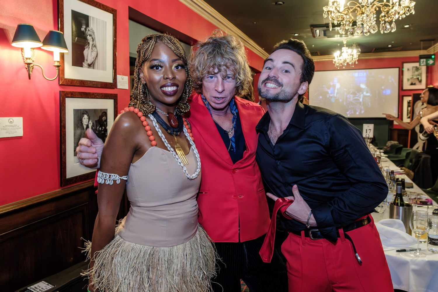 People celebrate and pose together in a dimly lit venue with red walls and chandeliers.