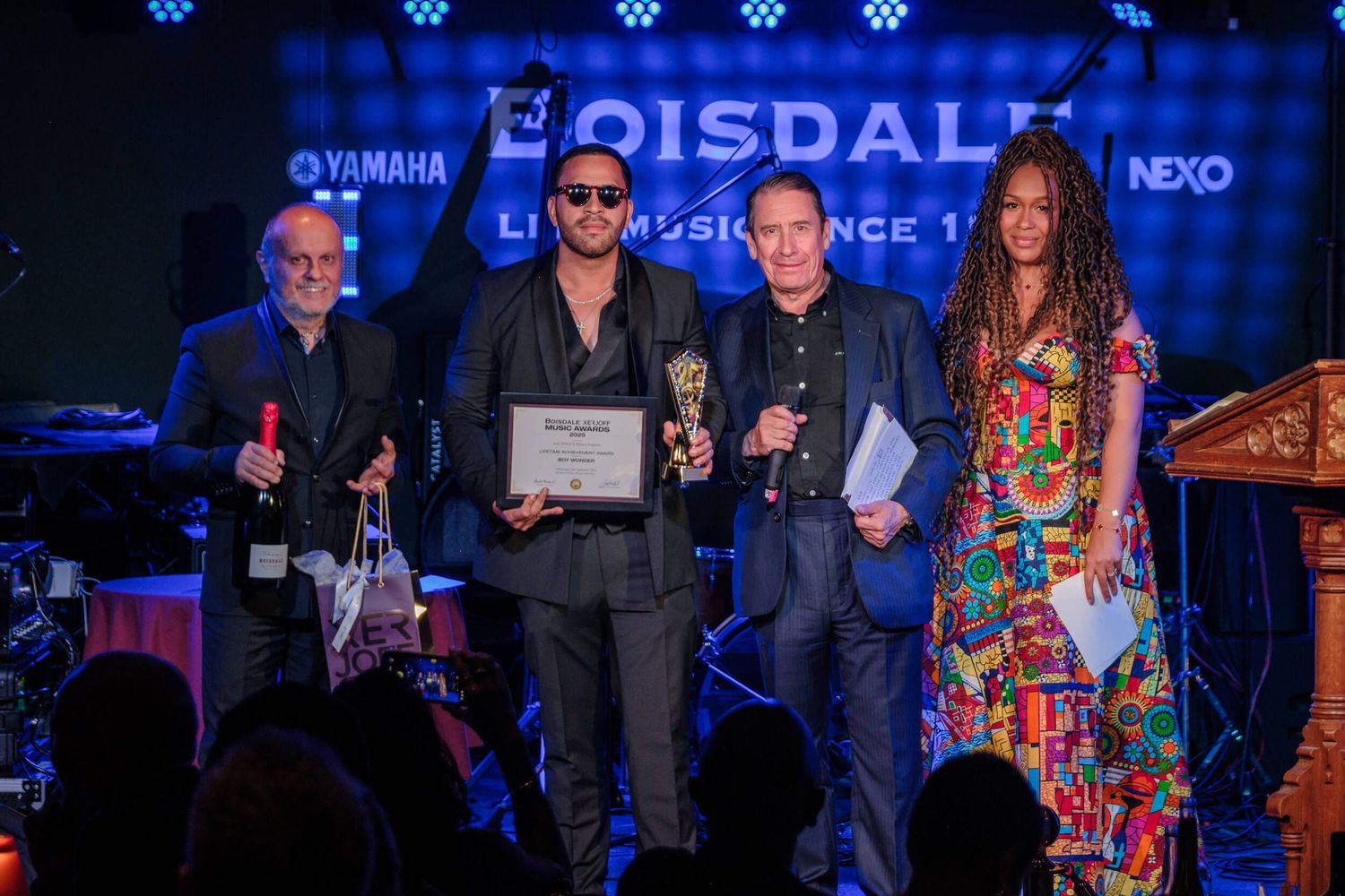 Musicians perform on stage at a concert with Yamaha and Nexo branding visible in the background lighting.