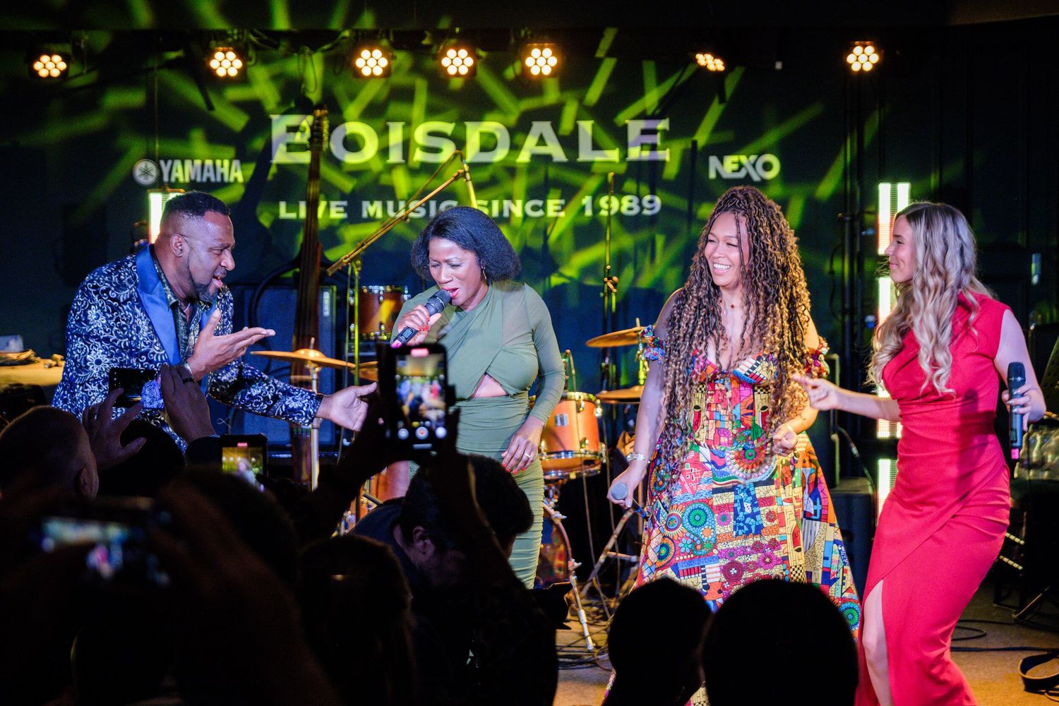 Performers on stage at a music venue with colorful lighting and instruments creating a lively atmosphere.