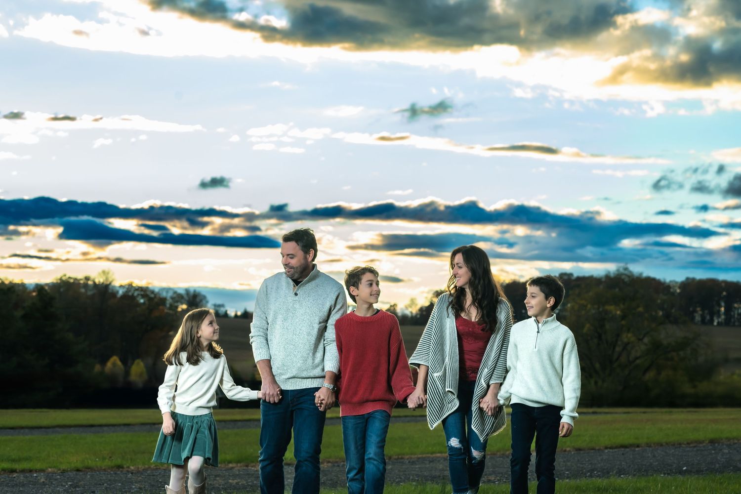 A group of people walking together across a field at sunset with dramatic cloudy skies overhead.