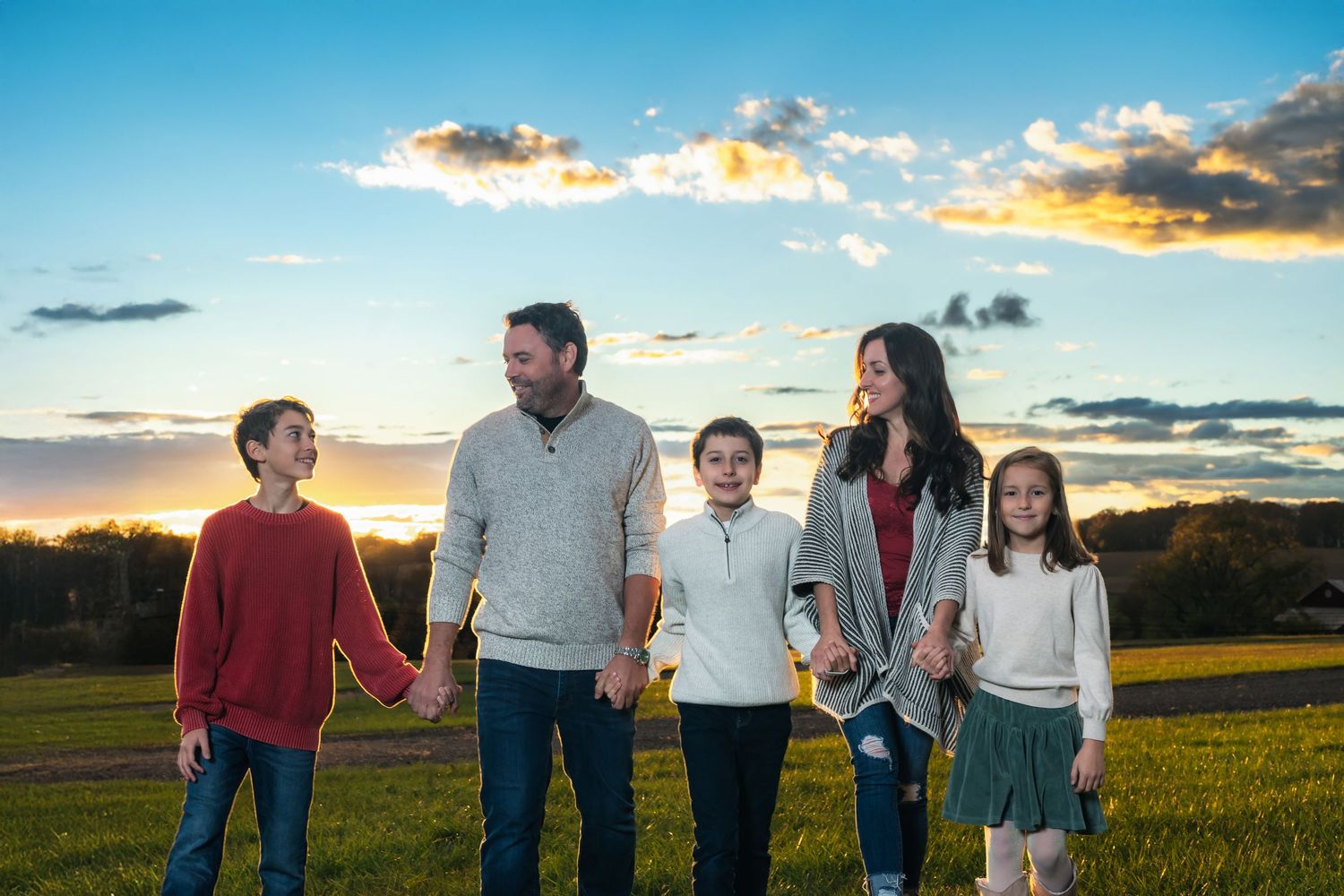 A family walks together through a golden field at sunset with dramatic clouds in the sky.