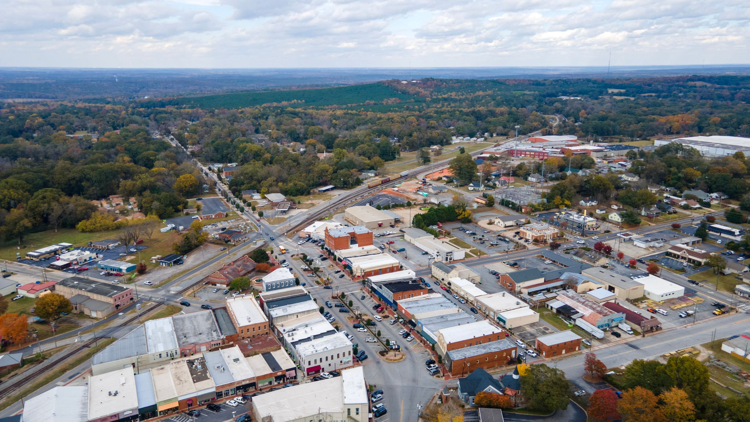 Aerial panoramic view of a small town with buildings and roads surrounded by rural farmland and forests.