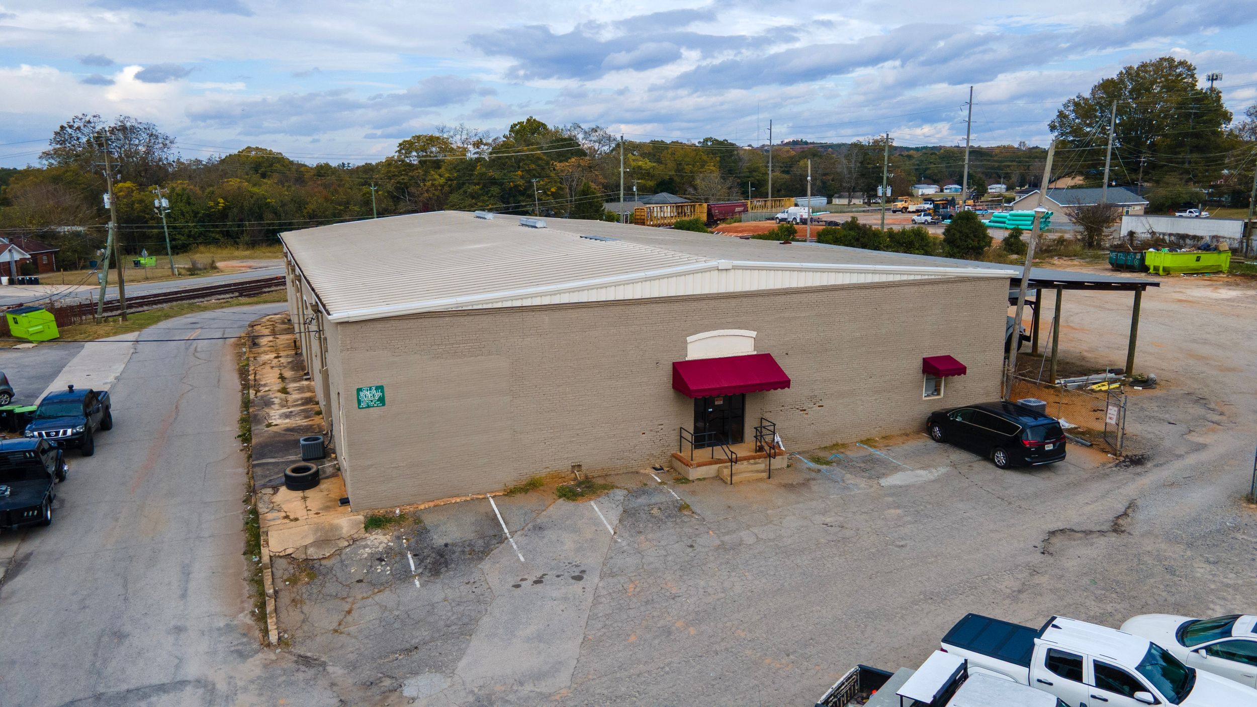 Aerial view of a commercial building with red awnings and parked vehicles in a paved lot.