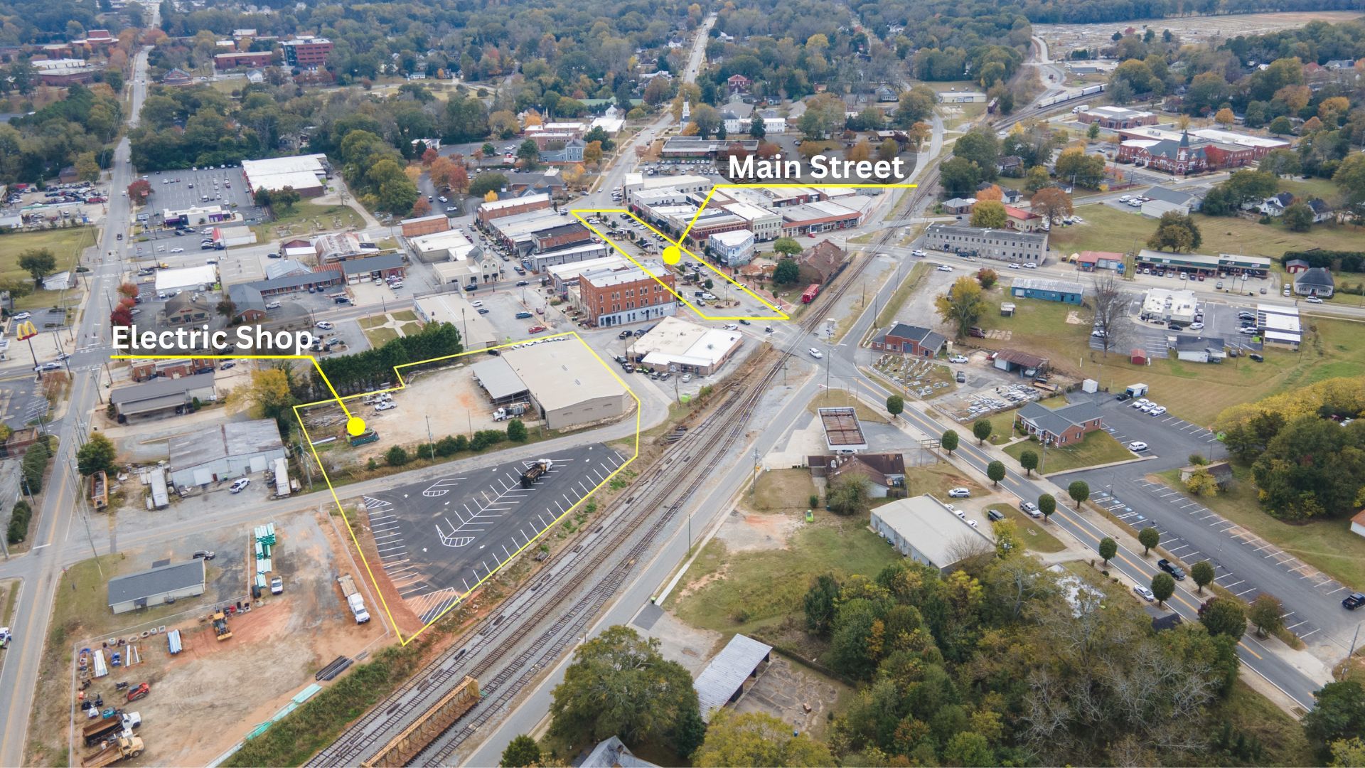 Aerial view of small town intersection with railroad tracks, businesses, and roads converging in rural setting.