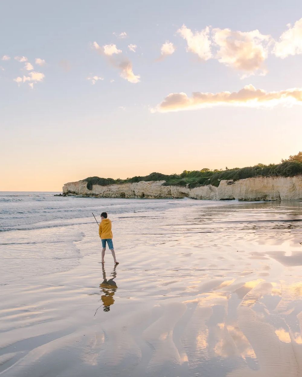 Child running along the beach at sunset with soft reflections on the wet sand.