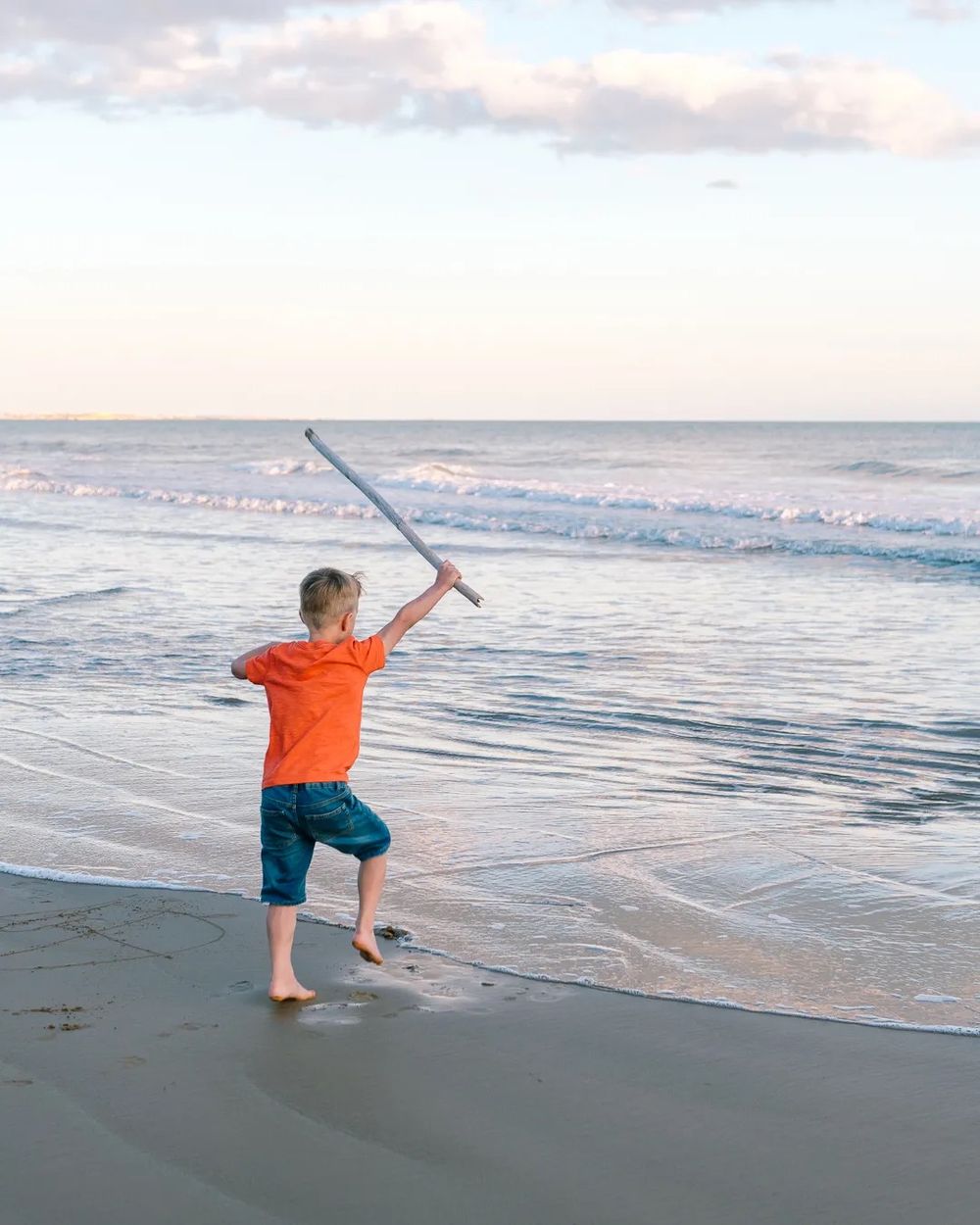 Boy playing with a fishing net on the shoreline as gentle waves roll in.