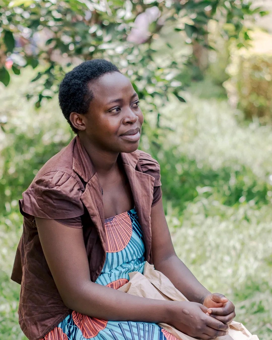Woman sits outside in a natural setting, appearing reflective and calm in a rural environment.