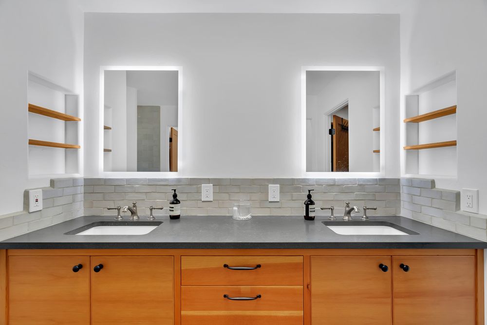 Contemporary bathroom vanity with wooden cabinets, dual sinks, and gray countertop under bright lighting.