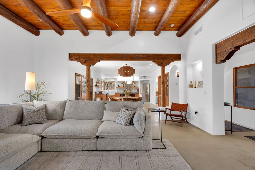 Modern loft-style interior with exposed wooden beams, white walls, and gray sectional sofa in an open floor plan.