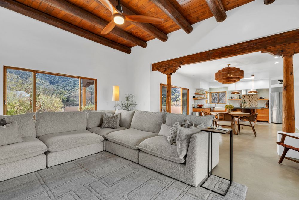 Contemporary living room with exposed wooden ceiling beams, gray sectional sofa, and mountain views.