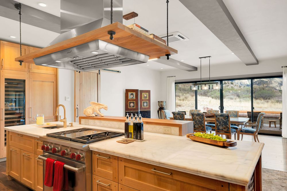 Modern open concept kitchen with wooden cabinets, pendant lights, and white countertops extending into a spacious living area.
