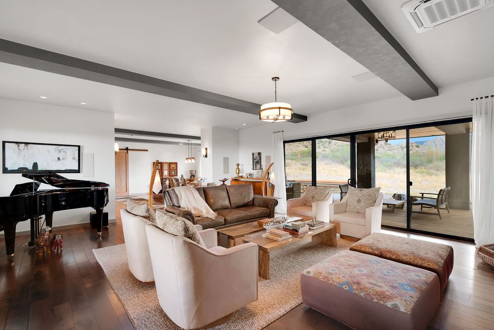 Modern living room interior with brown leather sofa, white armchairs, and hardwood floors in an open concept space.