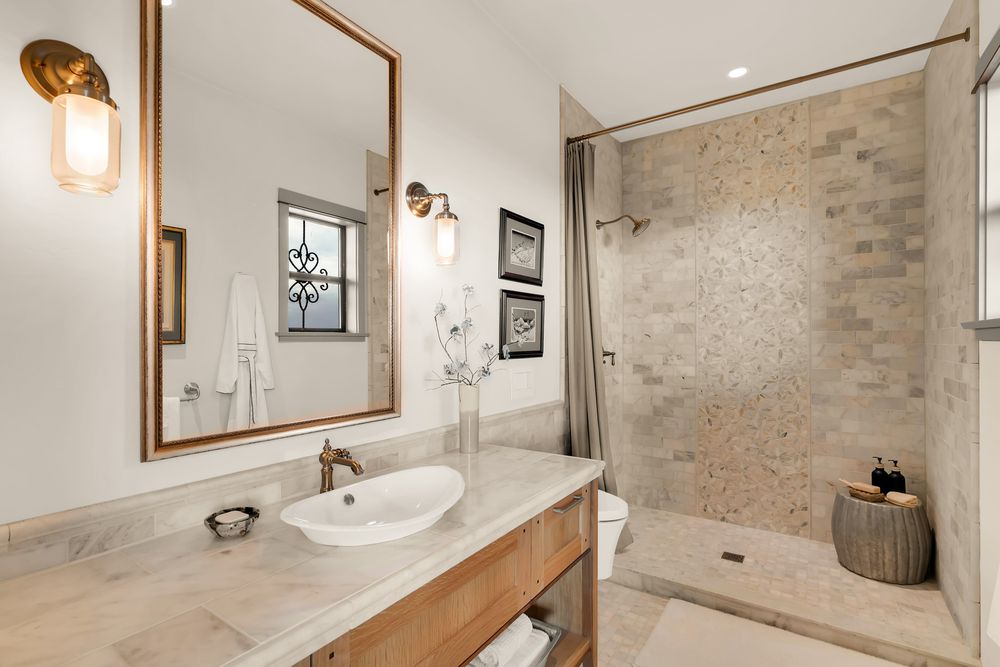 Modern bathroom with stone walls, wooden vanity, and elegant lighting fixtures features a sleek white bathtub.