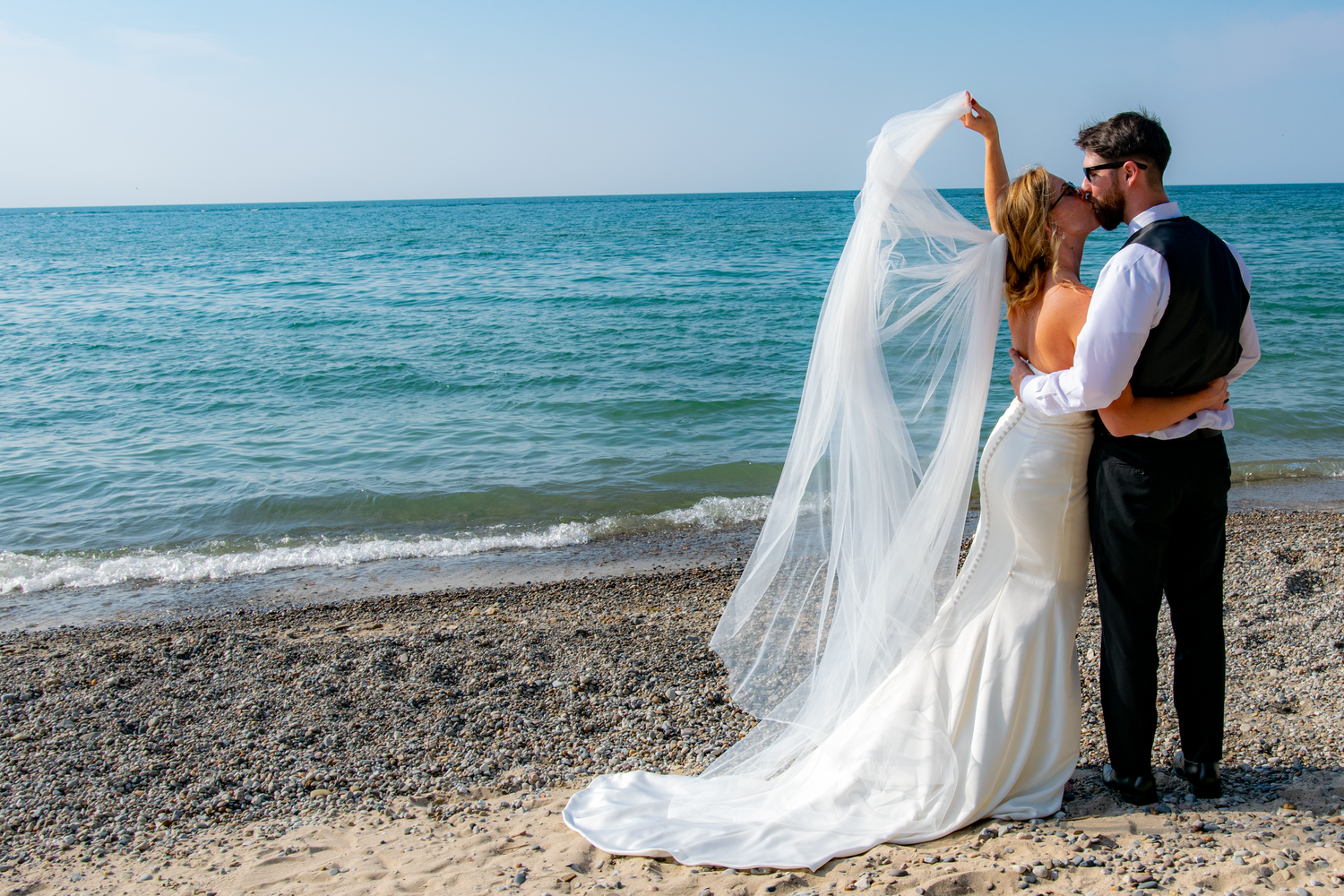 Newlyweds share intimate moments on a scenic beach with waves in the background.