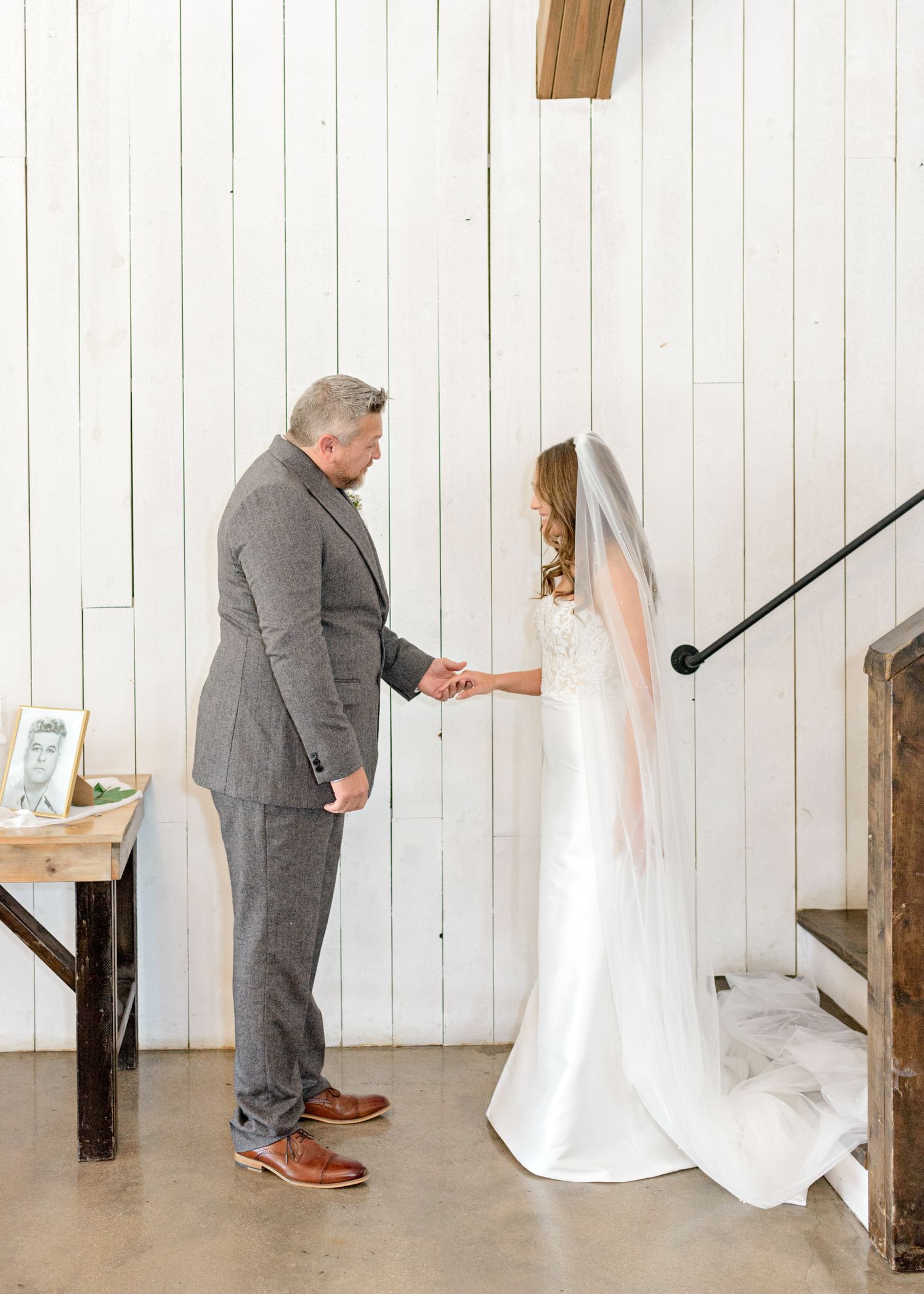 A touching first look moment between a bride in white and someone in a gray suit against white walls.