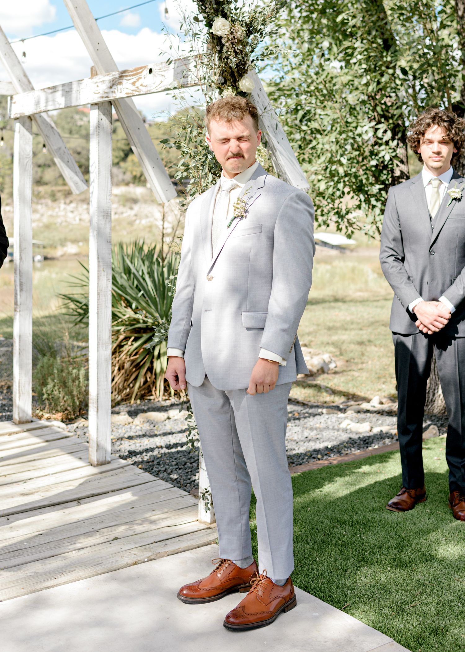 A formal wedding party stands at attention under a white pergola during an outdoor ceremony.