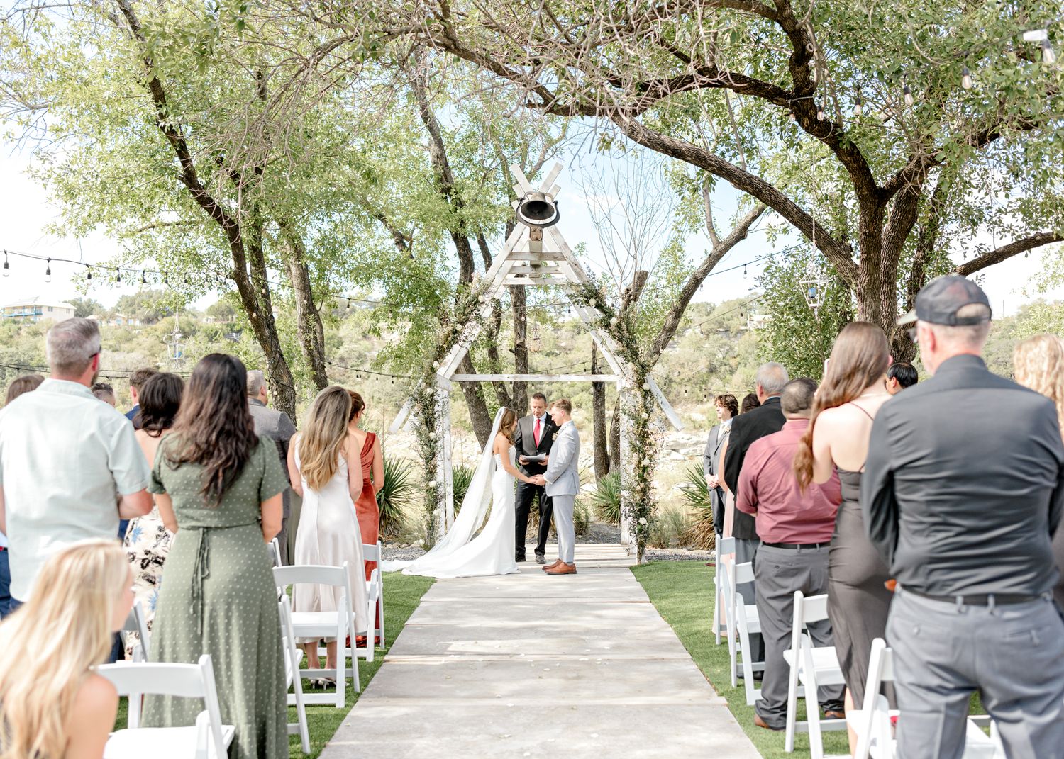 An outdoor wedding ceremony with guests seated along a white aisle leading to a decorated arbor.