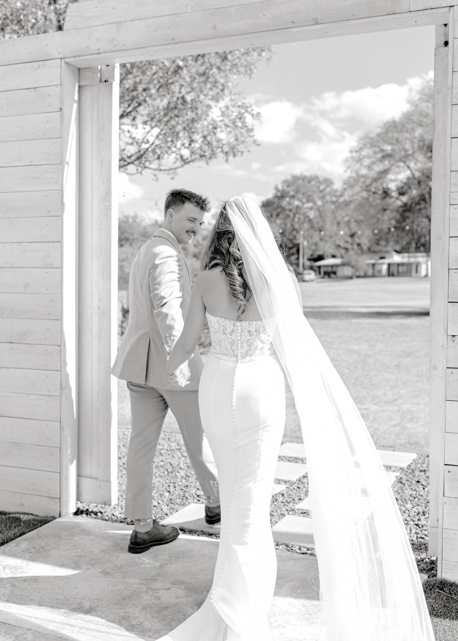 A black and white portrait of newlyweds sharing a moment outside a rustic white building.