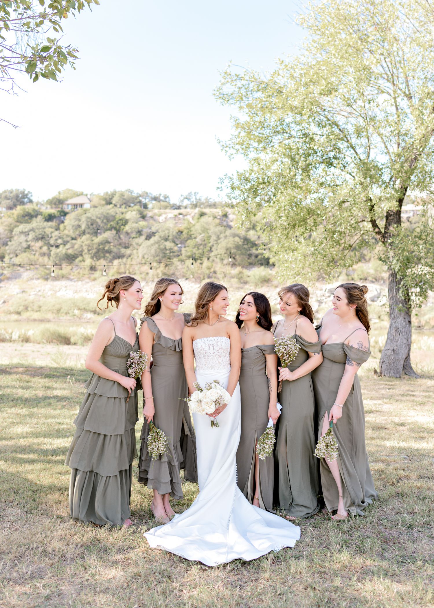 Bridal party in flowing gray dresses poses outdoors against a natural landscape.