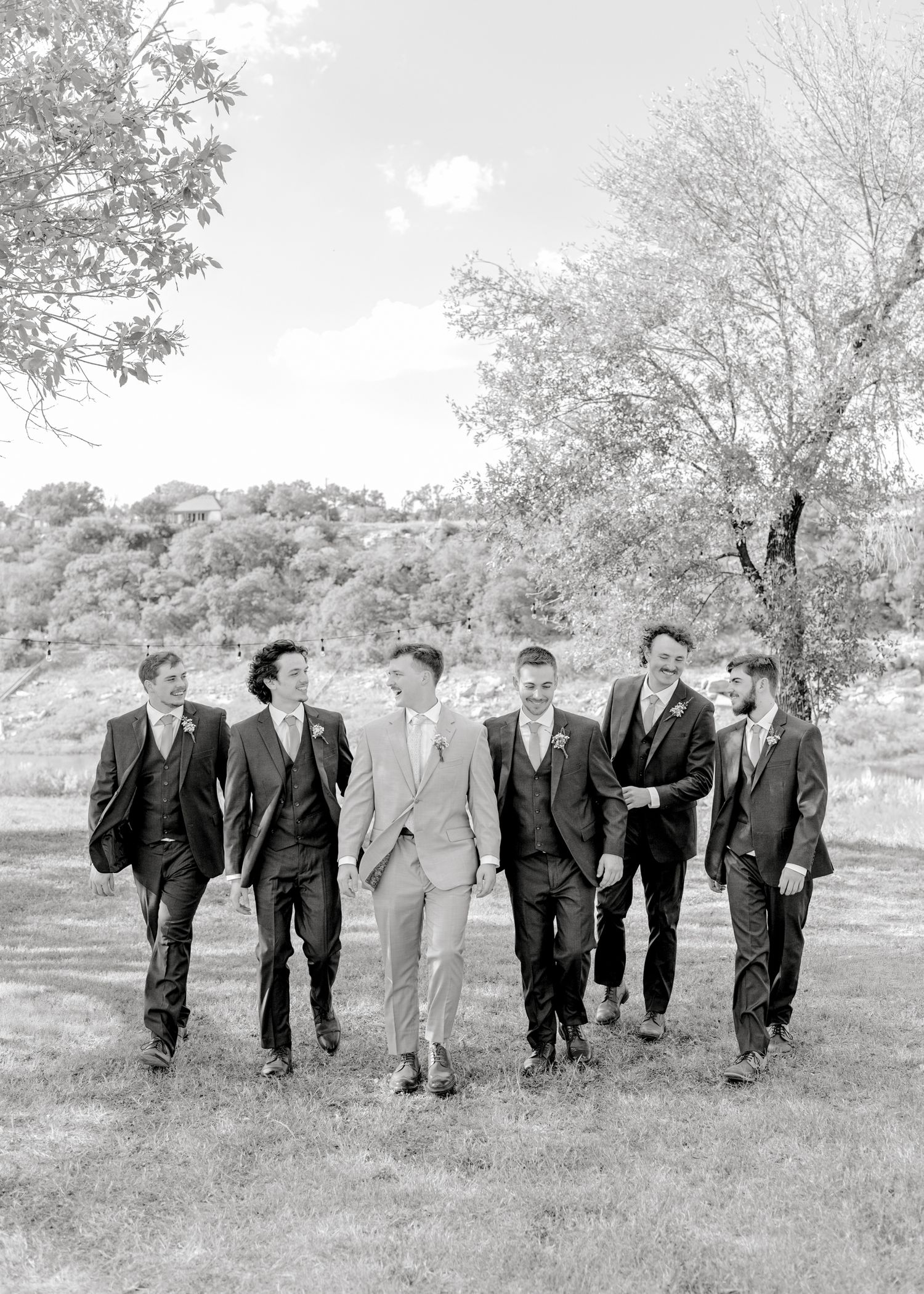 Black and white photo of groomsmen walking together through scenic outdoor venue.
