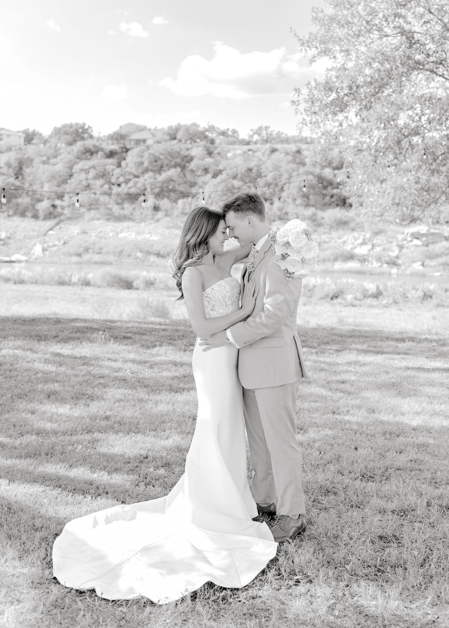 Black and white wedding portrait showing intimate moment in outdoor setting with flowing dress.