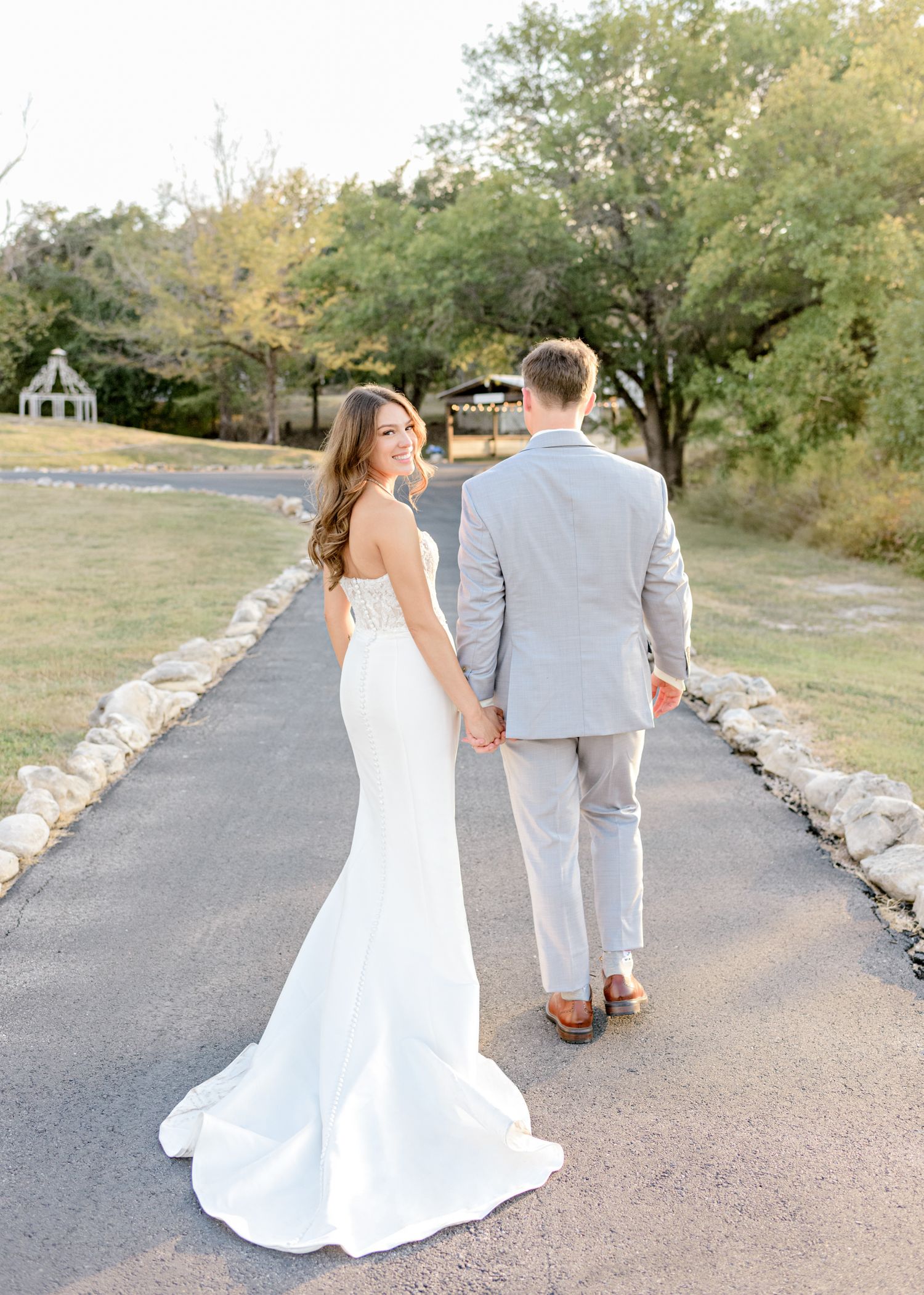 Wedding couple walks down stone-lined path with bride's dress trailing behind.