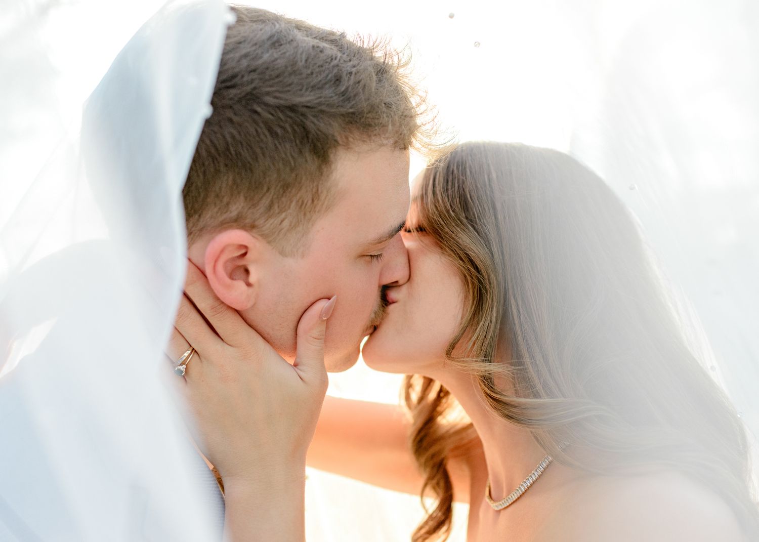 Romantic wedding portrait under veil with golden sunlight streaming through.