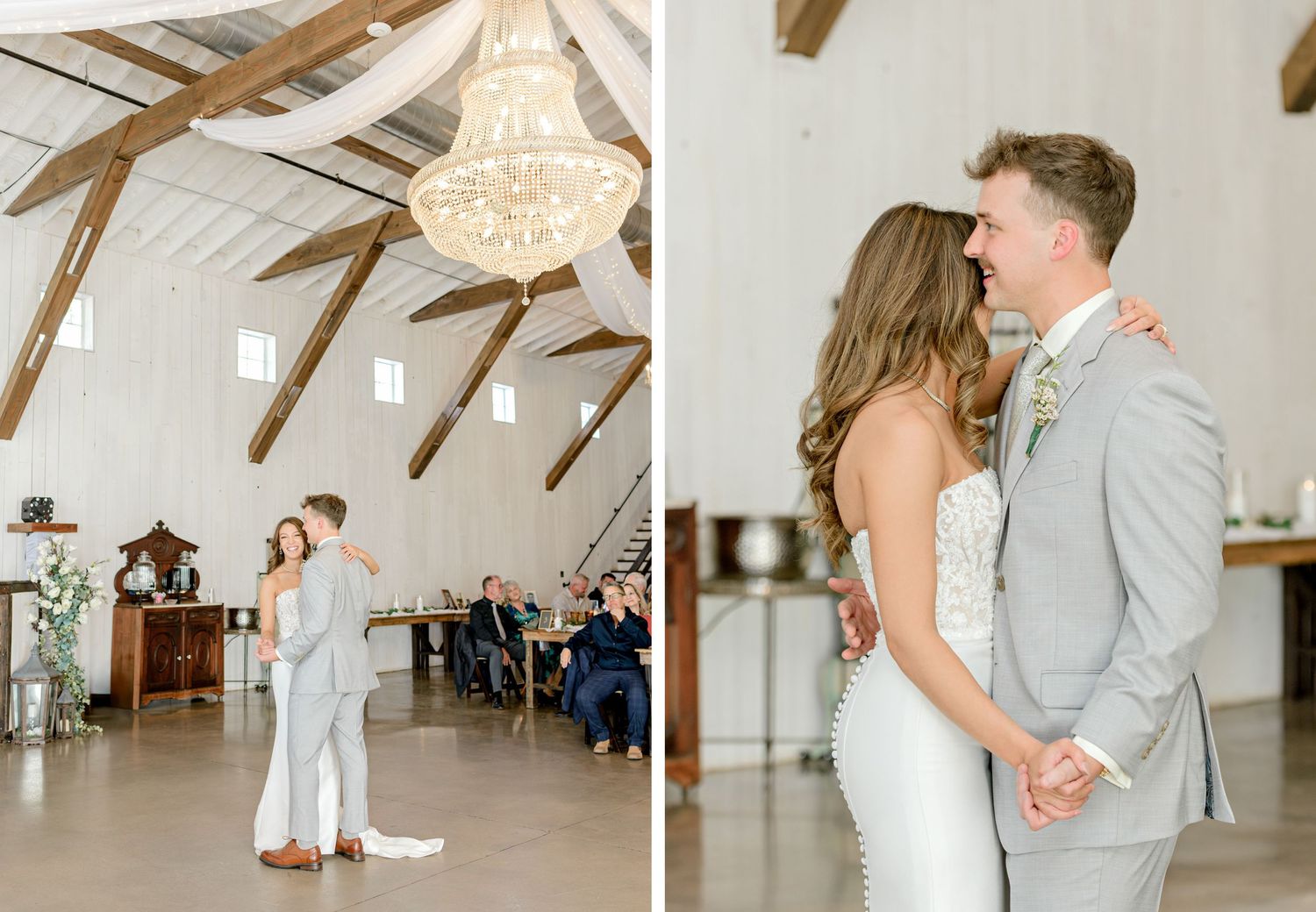 Wedding couple dances beneath crystal chandelier in rustic white barn reception venue.