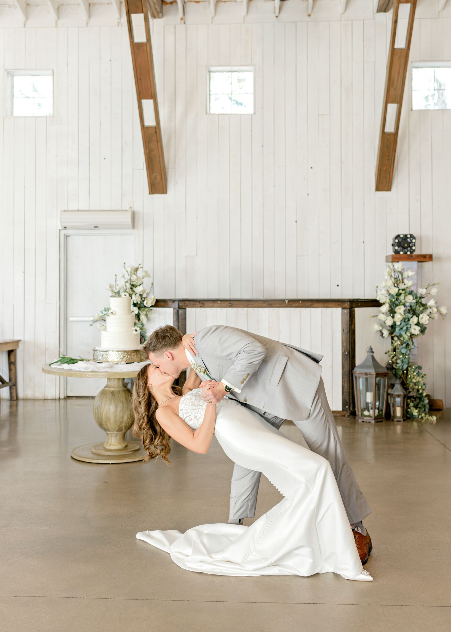 Couple performs romantic dance dip in bright white indoor venue with wooden beam details.