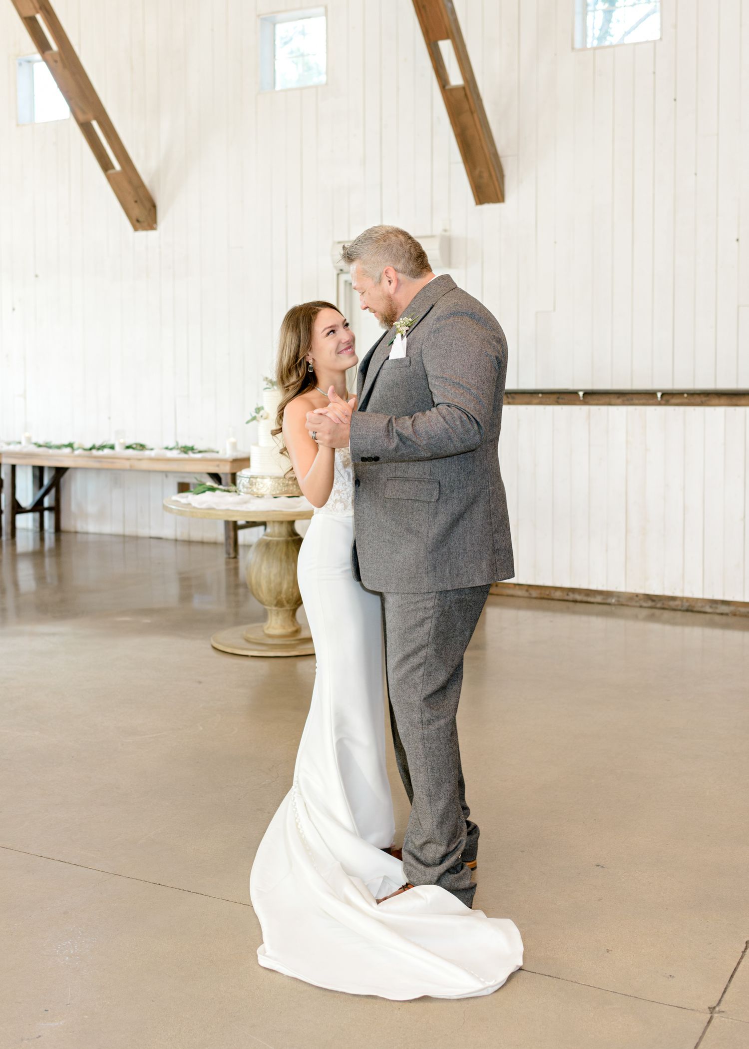 Intimate first dance moment captured in bright white barn venue with exposed wooden beams.
