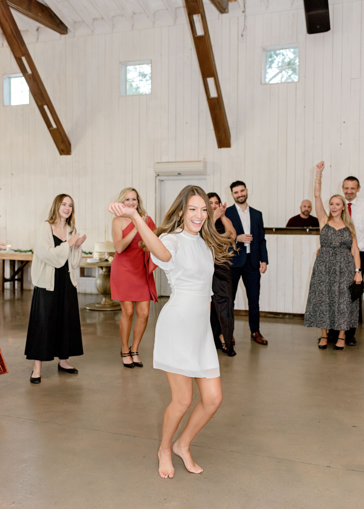 Dancers enjoying themselves at a wedding reception in a rustic venue with wooden beams and white walls.