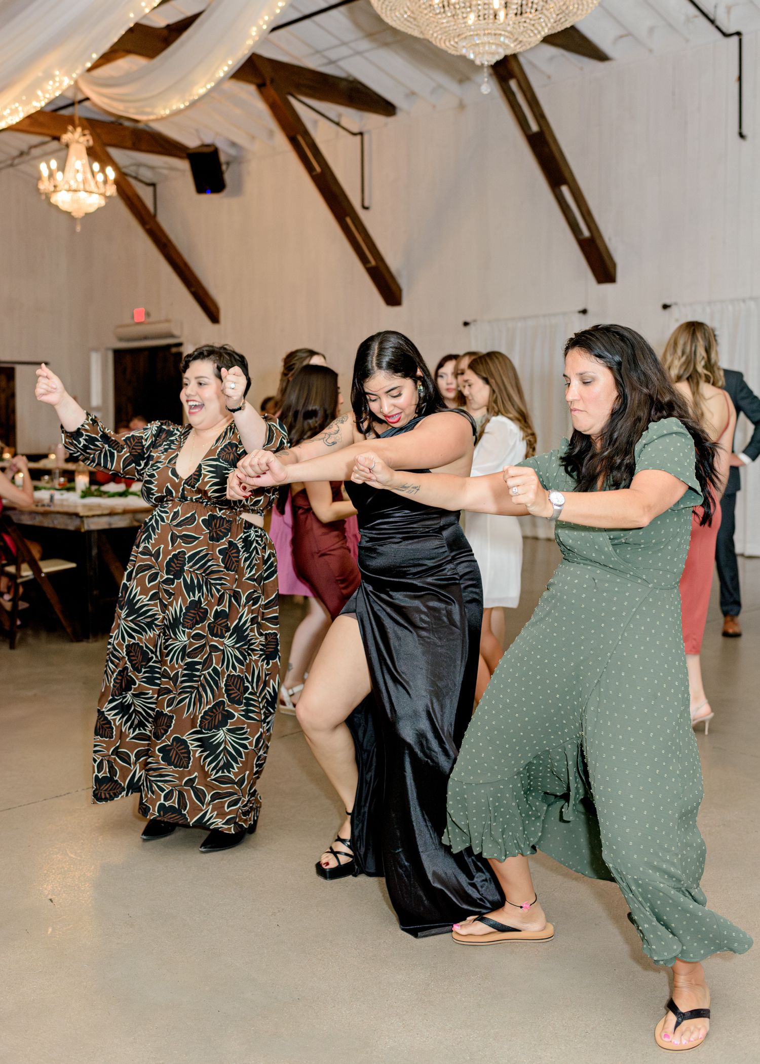 Group of wedding guests doing a coordinated dance move in a reception hall with chandeliers.