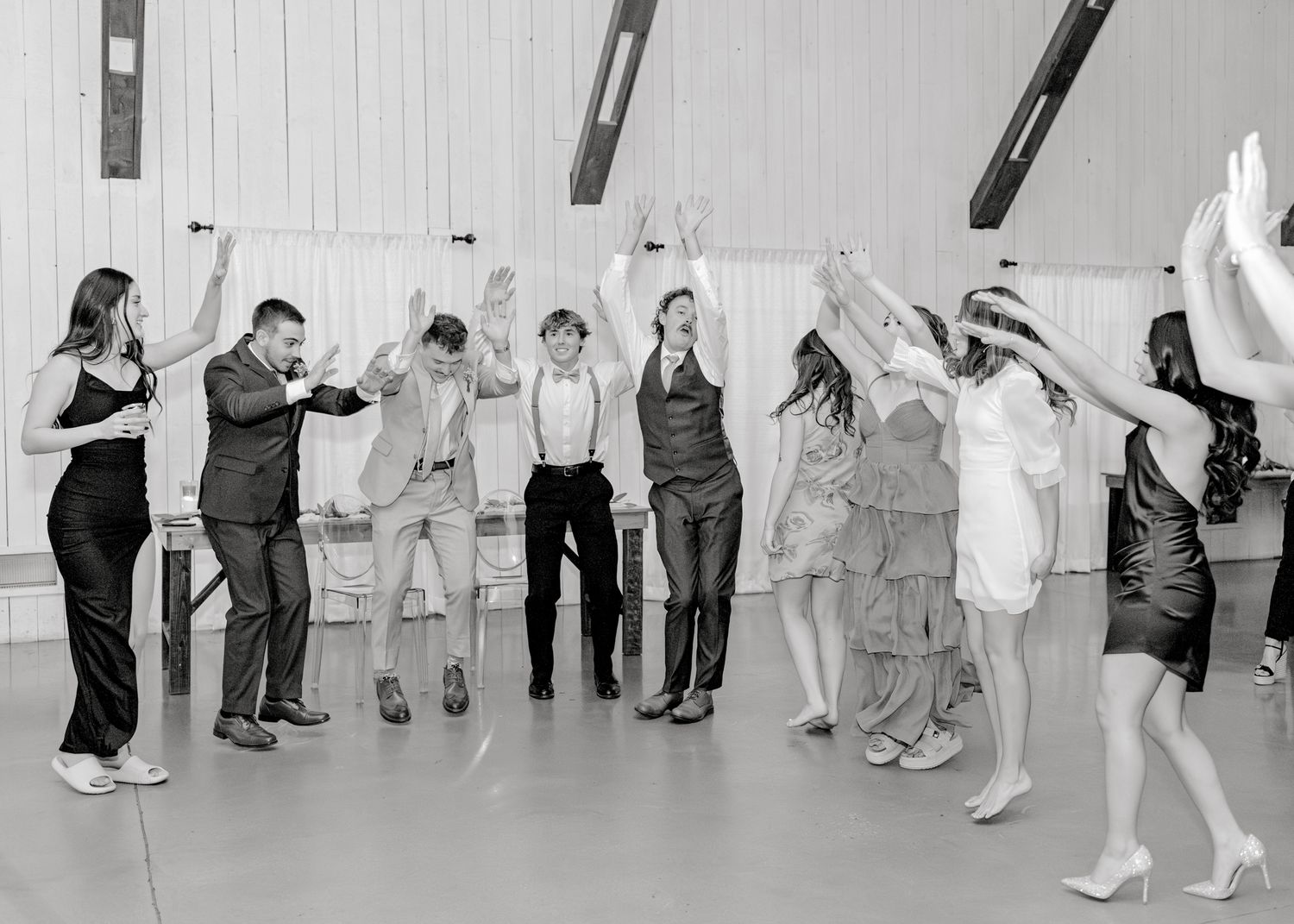 Black and white photo of wedding guests dancing and celebrating in a modern venue.