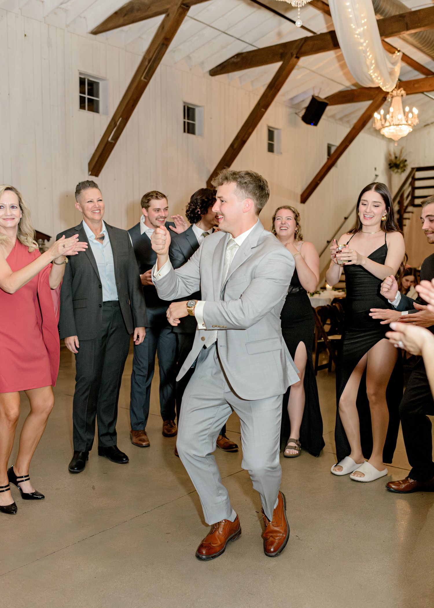 Guests dancing and celebrating at a wedding reception in a rustic venue with exposed beams.