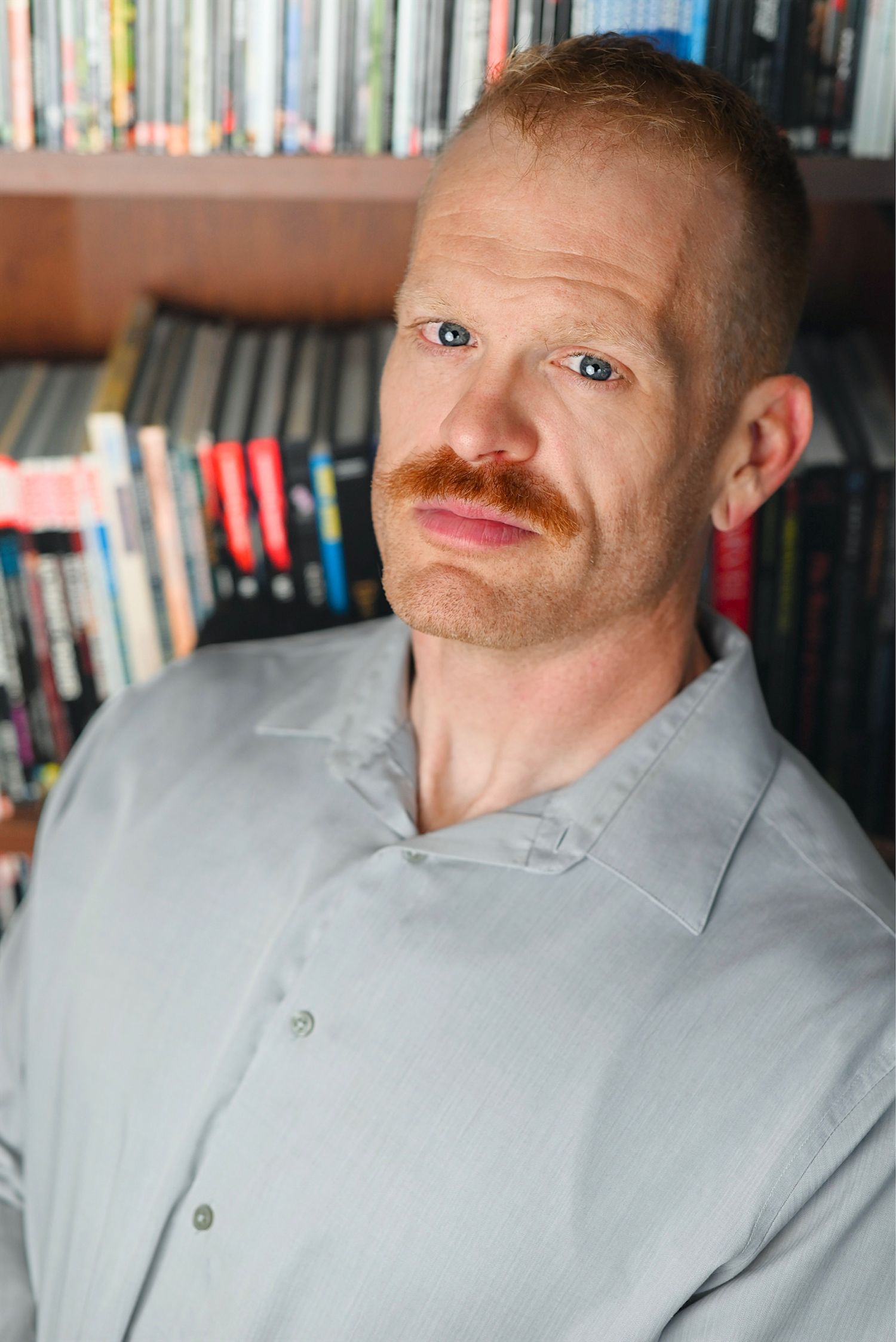 Portrait series featuring a ginger mustache and grey polo shirt against bookshelf background.