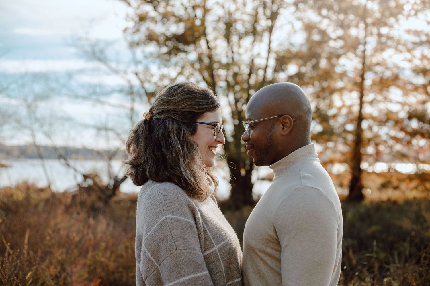 A romantic couple shares an intimate moment in autumn sunlight by a lake.