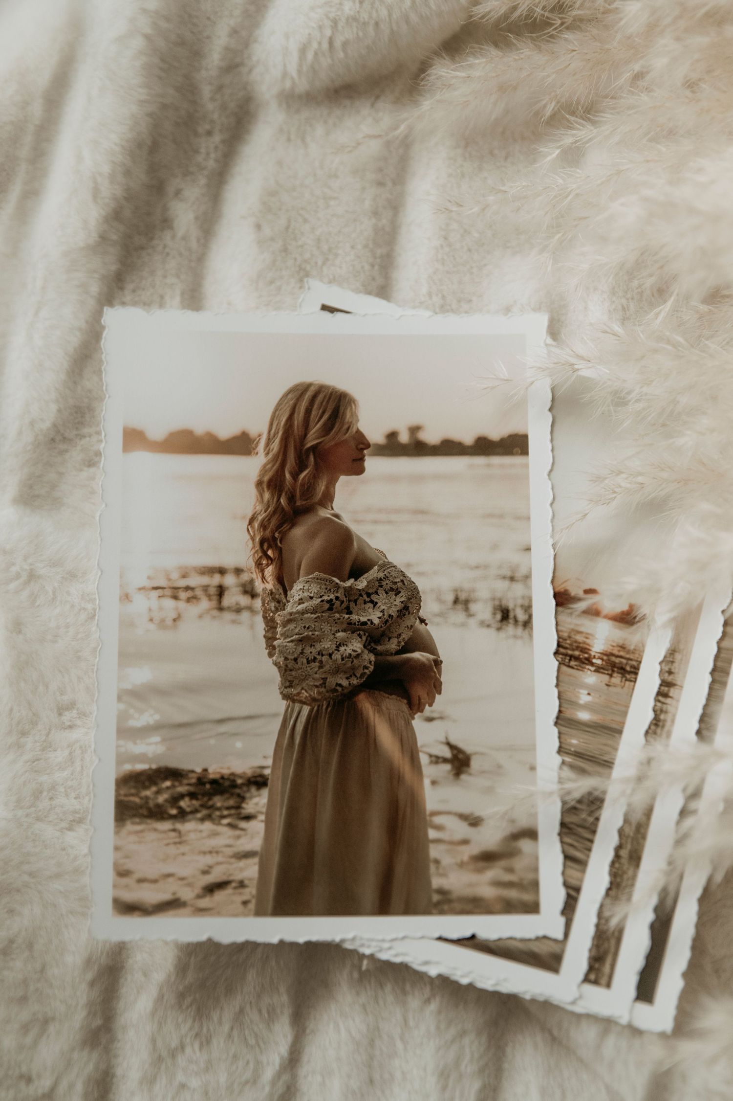 A vintage sepia photograph shows a figure in a flowy dress and cardigan standing by a waterfront at sunset.