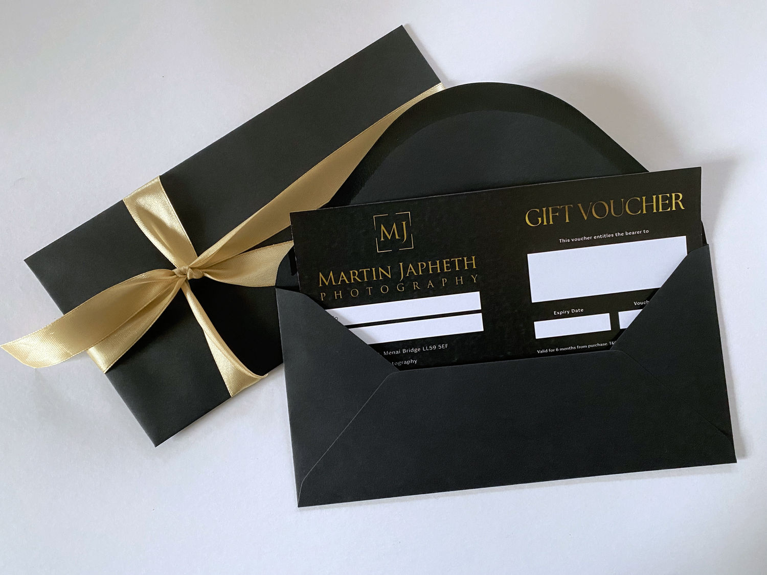 Black gift voucher envelope with gold ribbon and Martin Japheth branding.