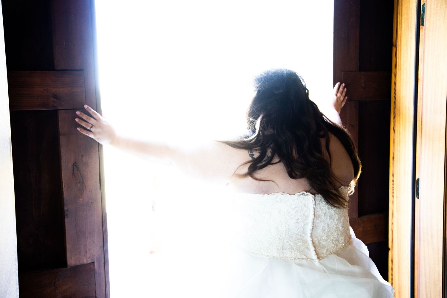 Silhouette of bride in wedding dress reaching toward bright doorway.