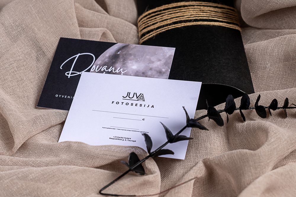 Business cards and black gift box arranged with dried eucalyptus on textured beige fabric.