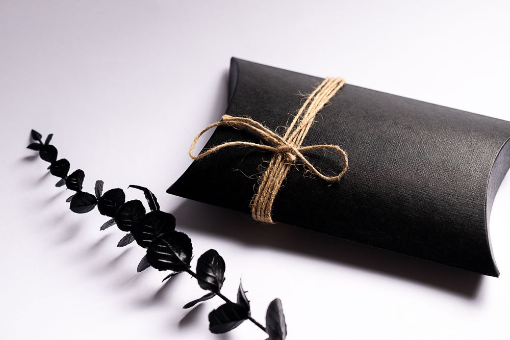 Black pillow box tied with twine string and decorated with eucalyptus sprig on white background.