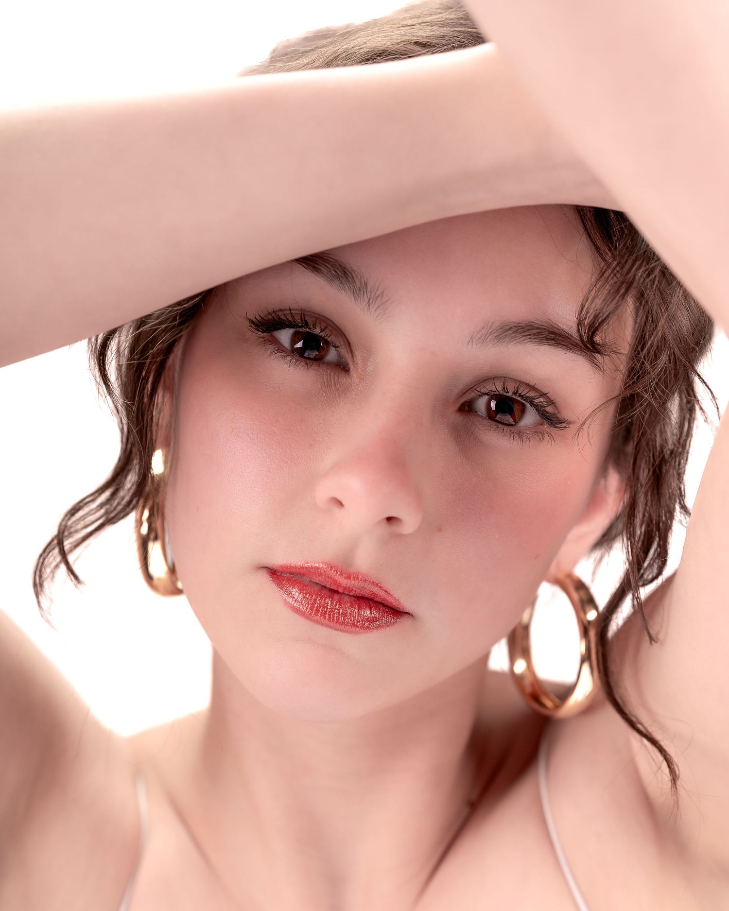 Portrait of someone with brown hair and red lipstick against a soft pink background.